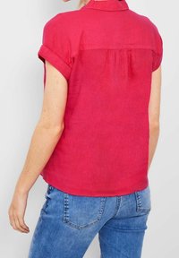 Rode blouse met korte mouwen van lichtgewicht stof, voorzien van een kraag en geplooide details aan de achterkant, gecombineerd met blauwe spijkerbroek.