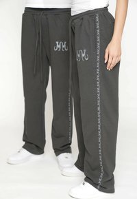 Grijze sweatpants met een elastische tailleband, zijzakken en decoratieve zilveren borduursels langs de buitennaad. Gestyled met witte schoenen.