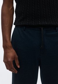 Σκούρα μπλε παντελόνι φόρμας από μαλακό, υφασμάτινο ύφασμα με ελαστική μέση και κορδόνι. Μερικώς ορατό μαύρο πλεκτό τοπ.