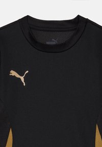 Fekete sporting, kerek nyakkivágással, hálós betétekkel és arany színű Puma logóval a bal oldalon. Simább textúra, légáteresztő kialakítással.