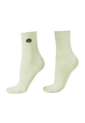 Světlé zelené kotníkové ponožky s žebrovanými manžetami, jedna ponožka má blízko kotníku malý vyšívaný obličej černohnědého psa.