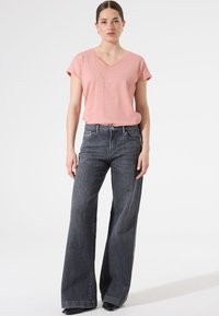 T-shirt rose pâle à col en V et manches courtes, associé à un jean large gris foncé. Tissu lisse avec un subtil éclat, design minimaliste.