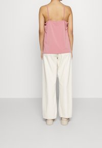 Top senza maniche di un tenue rosa chiaro con spalline sottili, abbinato a pantaloni bianchi a gamba larga. Il materiale sembra morbido con una vestibilità rilassata e senza fantasie.