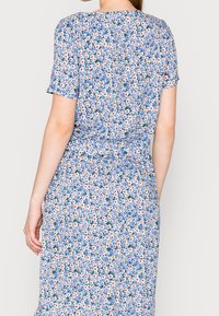 Abito floreale con uno sfondo blu decorato con piccoli motivi di fiori gialli, bianchi e arancioni, maniche corte e una vita arricciata.