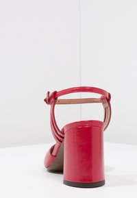 Sandale à talon haut en cuir verni rouge avec un talon épais, dos ouvert et bride de cheville. Texture lisse avec une finition brillante.