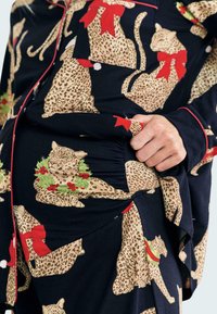 Black fabric pajama set featuring leopard print with red bows and green wreaths, accented by red piping. Soft, stretchy material.