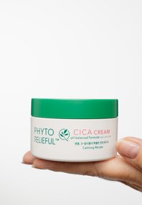 Rund vit burk med Cica-kräm och ett grönt lock. Texten på burken inkluderar "Phyto Reliefful" och "pH-balanserad formula." Slät yta.