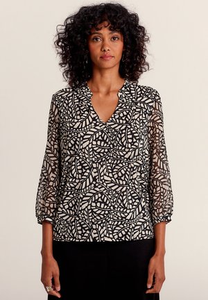 Zwarte en crèmekleurige blouse met een V-hals en driekwartmouwen. De stof is doorschijnend en heeft een bladmotief.
