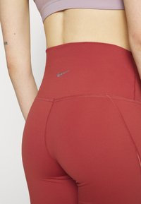 Leggings de sport taille haute en bourgogne, fabriqués en tissu extensible, présentant un logo Nike argenté et des coutures à plat pour le confort.