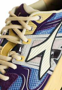 Sneaker sportivo con una tomaia multicolore nei toni del blu, viola e giallo. Presenta materiali testurizzati, lacci a contrasto e un dettaglio logo prominente.