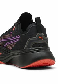 Chaussure de sport noire avec tige en mesh ornée d'accents violets et oranges, col rembourré et semelle en caoutchouc noire texturée avec des détails rouges.