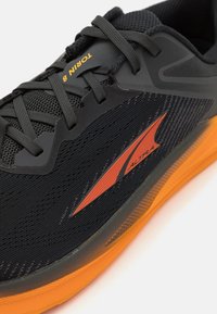 Foulée noire avec tige en mesh, accents orange et semelle extérieure texturée. Lacets bien serrés, avec la marque "Torin 8" sur le côté.