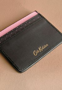 Juodas kortelių laikiklis su rožiniais akcentais ir taškuotais raštais. Apačioje įspaustas auksinis logotipas "Cath Kidston". Lygus paviršius, stačiakampio forma.