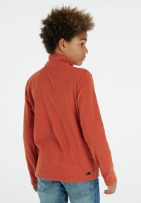 Pullover arancione in felpa con colletto alto, caratterizzato da una texture morbida e una piccola etichetta con logo sull'orlo. Visto da dietro.