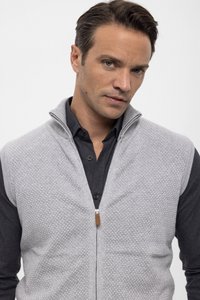 Gilet grigio chiaro con zip, motivo testurizzato, materiale in maglia, colletto alto e camicia scura a contrasto sotto. Hardware marrone sottile.