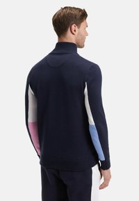 Pull marin avec un grand col, présentant un design coloré en blocs de rose, blanc et bleu clair sur les manches, avec des poignets et un ourlet côtelés.