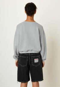Felpa grigia chiara oversize con texture a costine, abbinata a pantaloni corto in denim neri con orli grezzi e una toppa con logo sul retro.