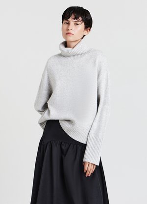 Maglione a collo alto grigio chiaro con polsini e orlo a costine, abbinato a una gonna nera. Il maglione ha una vestibilità rilassata e una consistenza morbida.