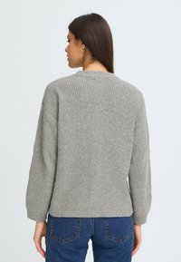 Sivi pleteni pulover z rebrasto teksturo, okroglo ovratnikom in spuštenimi rameni. Dopolnjujejo ga temno modri kavbojke.