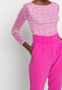 Långärmad topp i rosa och vit abstrakt mönster, matchad med högmidjade, ljusrosa byxor med bälte och skräddarsydd passform.