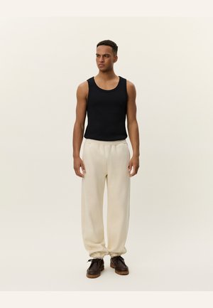 Sort bomulds tank top, creme farvede brede bukser, brune sko med snørebånd. Bukserne har elastiske manchetter. Simpelt, afslappet design uden mønstre.