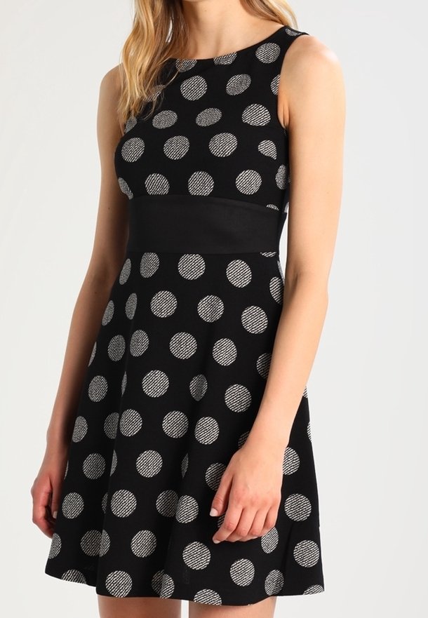 Musta hihaton mekko, jossa on suuret valkoiset pilkut, istuva vartalonmukainen yläosa ja levenevä hameosa. Valmistettu teksturoidusta kankaasta, jossa on vyötäröyksityiskohta.