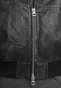 Černá kožená bomber bunda s výrazným stříbrným zipem a žebrovanými manžetami, která se vyznačuje hladkou texturou a klasickými designovými prvky.