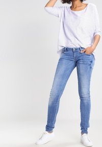 Pruhovaný top s dlouhými rukávy v purpurové a bílé barvě spárovaný se světle modrými skinny džíny a bílými teniskami. Každodenní a přiléhavý design s uvolněným střihem.