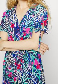 Abito con stampa floreale su sfondo blu navy, caratterizzato da vivaci tonalità di rosa e verde, maniche corte con lacci e profondo scollo a V.
