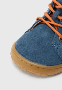 Sötétkék színű, bőrhatású cipő gumitalppal és narancssárga fűzőkkel. Kerek orral és texturált felsőrésszel rendelkezik, kontrasztos varrással és fém szemekkel.