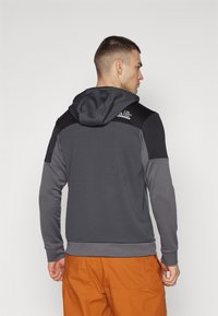 Felpa con cappuccio realizzata in tessuto grigio testurizzato con dettagli neri sulle spalle. Presenta una patch con il logo sulla parte posteriore e polsini a costine.