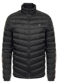 Mustapuffatakki, jossa on korkea kaulus, tikattu muotoilu, etuvetoketju ja logo vasemmassa rinnassa. Miellyttävä, kiiltävä pinta ja istuva muoto.