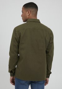 Olive green button-up shirt with long sleeves and a collar, made from cotton fabric. Features visible stitching and a classic fit.