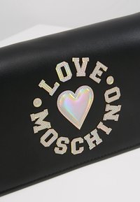 Svart läderplånbok med "LOVE MOSCHINO" i metalliska bokstäver, med en holografisk hjärtdekoration och dekorativa rhinestones.