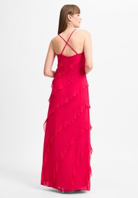 Maxikleid aus leuchtend pinkem Chiffon mit gestuften Rüschendetails und überkreuzten Trägern auf der Rückseite, das ein fließendes Design und ein leichtes Material zeigt.