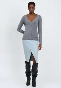 Grauer V-Ausschnitt-Cardigan mit Knöpfen, kombiniert mit einem hellblauen Denim-Rock mit einem Schlitz an der Vorderseite und knielangen, schwarzen, slouchy Stiefeln.