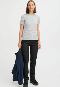 T-shirt grigio chiaro a maniche corte abbinato a pantaloni cargo neri. Giacca in pile blu navy tenuta nella mano sinistra, dotata di zip.
