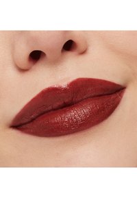 Tiefroter Lippenstift auf glatten Lippen, mit einem glänzenden Finish und klar definierten Konturen, vor einem hellen, gleichmäßigen Hautton.
