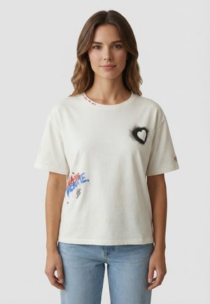 Donna con capelli castani che indossa una maglietta bianca con grafica a cuore nero e testo colorato, abbinata a jeans azzurri.