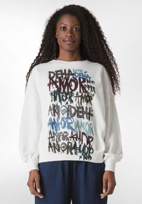 Sudadera blanca con un diseño de texto colorido en diferentes tipografías, incluyendo "AMOR", con un ajuste relajado y mangas con puños.