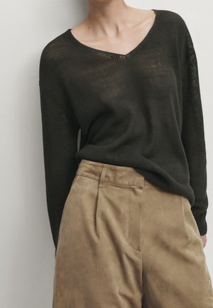 Dark green, textured knit sweater with a V-neck and long sleeves, paired with tan, suede, high-waisted pants featuring pleats.