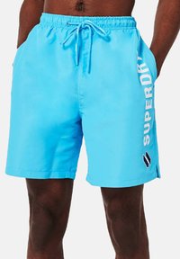 Bañador azul hecho de material ligero, con una cinturilla elástica con cordón y un logo blanco en el lado.