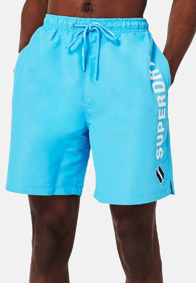 Bañador azul hecho de material ligero, con una cinturilla elástica con cordón y un logo blanco en el lado.