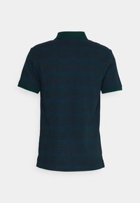 Polo bleu foncé à manches courtes avec un col vert et des bordures de manches vertes, vu de dos sur un fond clair et uni.