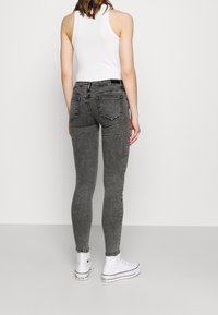 Jeans grises, ajustados y fabricados en denim, con una cintura alta, bolsillos traseros y un acabado desgastado, combinados con zapatillas blancas.