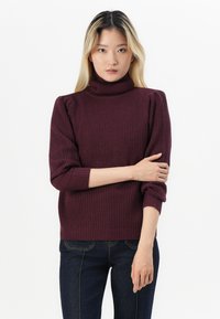 Burgundy stickad polokrage med ribbad textur; har puffärmar och åtsittande manschetter. Tillsammans med mörkblå jeans.