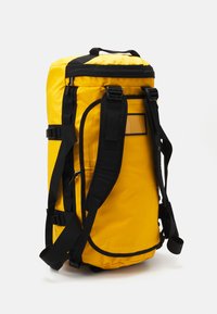 Zaino da esterno giallo brillante con spallacci imbottiti neri, maniglia superiore, più fibbie e cinghie di compressione laterali su uno sfondo bianco.