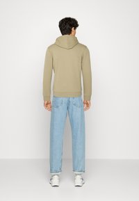 Sudadera beige con capucha, puños y dobladillo acanalados, combinada con jeans rectos de color azul claro. Textura suave y diseño sencillo.