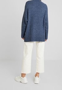 Maglione blu lavorato a maglia con una vestibilità ampia e orlo a coste, abbinato a pantaloni larghi color crema e sneakers bianche. Tessuto liscio, design casual.