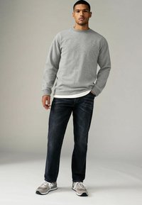 Hall keerukes gris sweatshirt ribitud varrukatega, valge särgi peale pandud. Kombineeritud tumeda sinise teksapükstega ja hallide tossudega, millel on valged aktsendid.